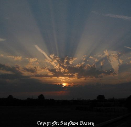 The suns rays radiate from behind the clouds
